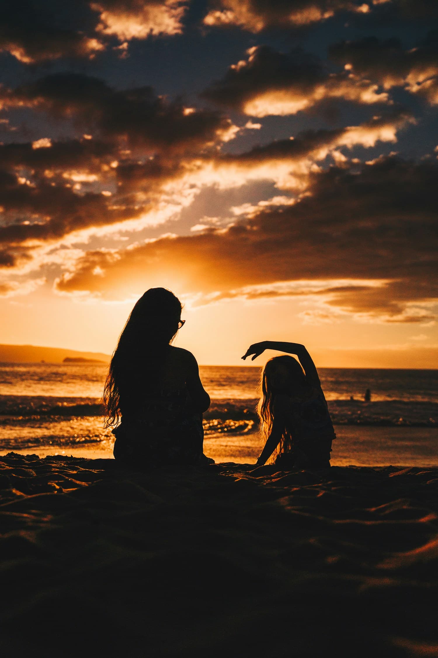 An adult and child sitting together at sunset